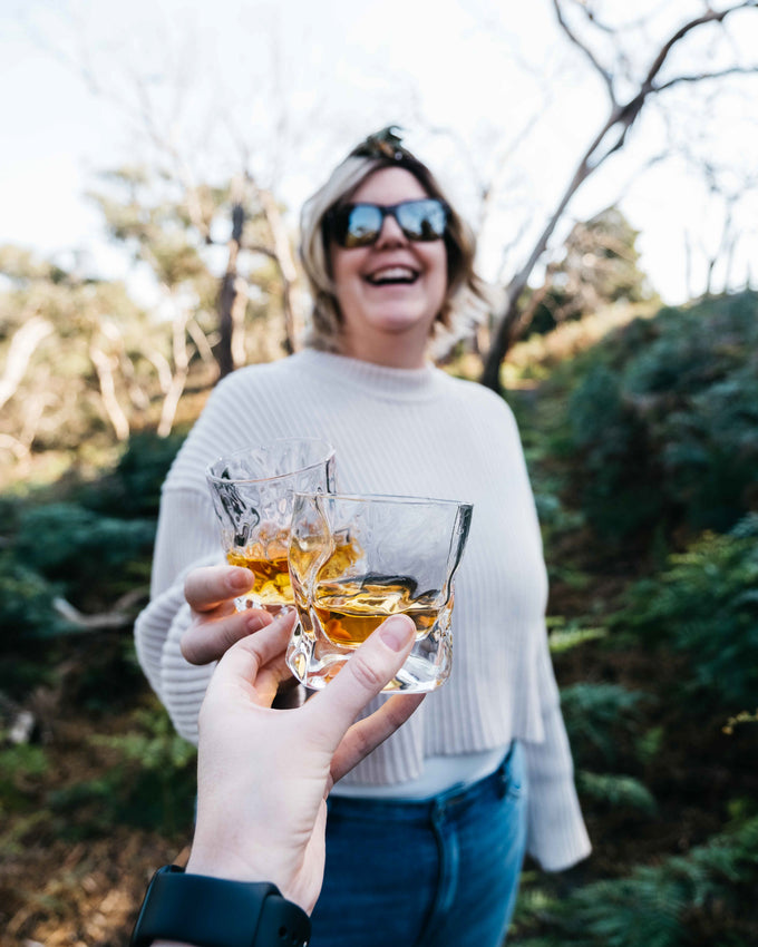 A woman clinks a Malt & Brew glass with the cameraperson in celebration.